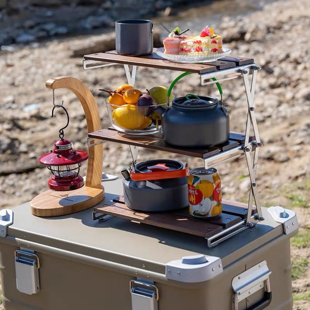 The versatile Super Wooden Desk Shelf is deployed on a cooler in a camping setting, holding a kettle, fruit, cake, and a lantern | Cyber Vintage