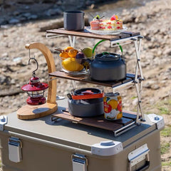 The versatile Super Wooden Desk Shelf is deployed on a cooler in a camping setting, holding a kettle, fruit, cake, and a lantern | Cyber Vintage